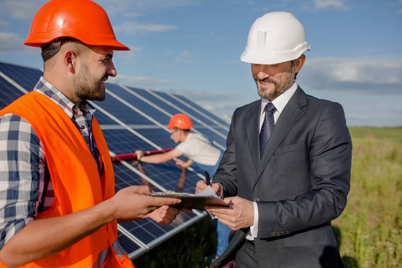 Two men shaking hands in front of a solar panel
