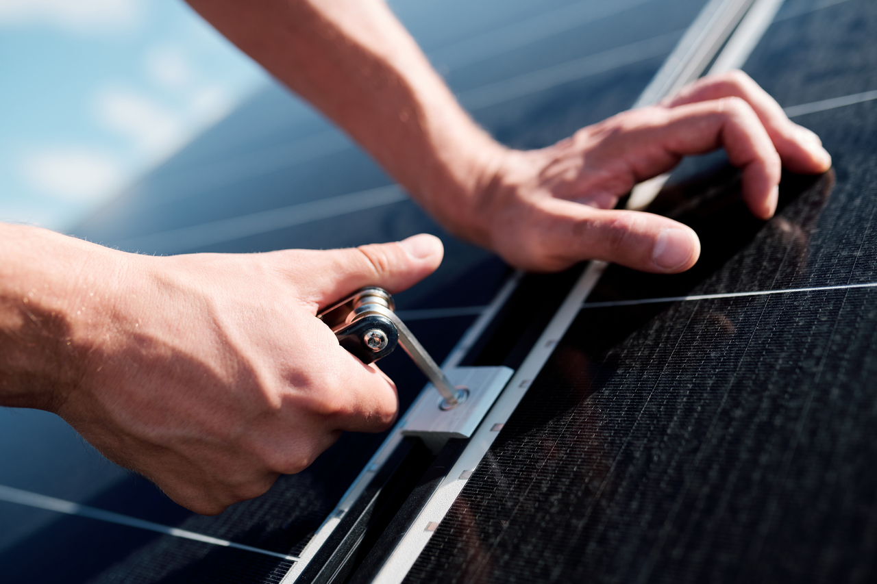 A solar technician's hands screwing a bolt into a solar panel